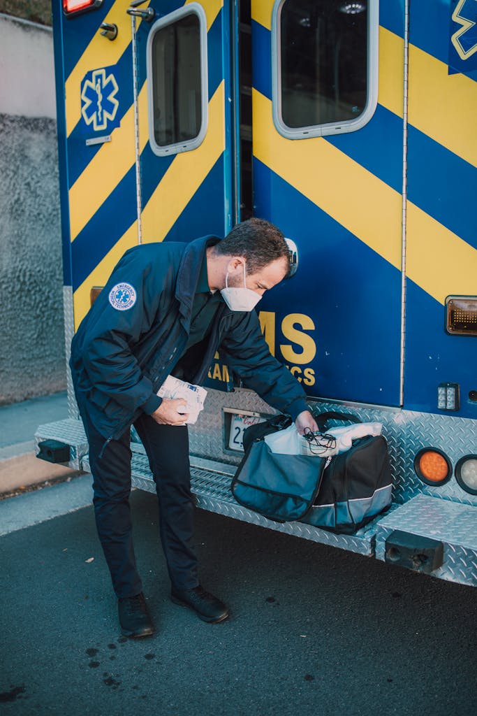EMT gathers gear from ambulance for emergency response outdoors.