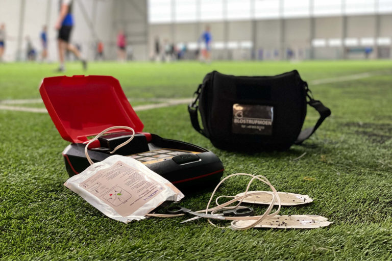 En hjertestarter som er brukt i en hendelse. Elektrodene viser at den er full ab kroppshår og skitt. Den ligger på en kunstgressbane der den ble brukt.